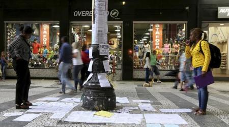Unas personas observando anuncios de empleos pegados en un poste en Sao Paulo