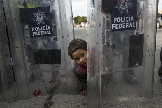 Niño migrante juega detras de escudos policiales en la frontera con EEUU