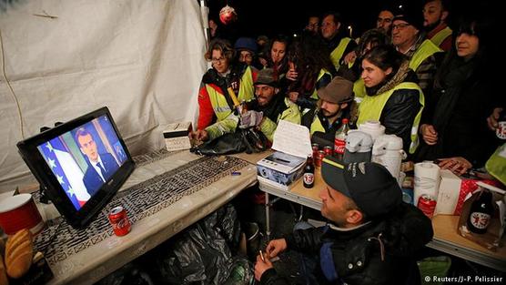 Manifestantes observan a Macron por la tele