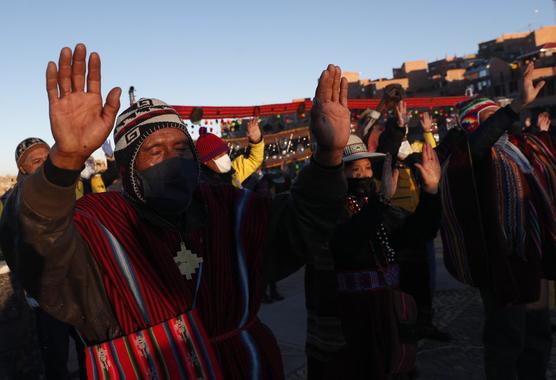 Los indígenas aymaras con máscaras faciales de protección levantan sus manos ante los primeros rayos de sol de ayer domingo