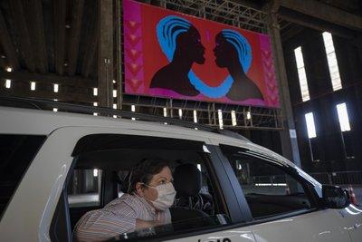 Una mujer con una mascarilla para protegerse del coronavirus observa una exposición artística desde un auto