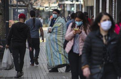 Un hombre sin hogar que usa una mascarilla para prevenir el nuevo coronavirus pide monedas a peatones en una calle de Santiago